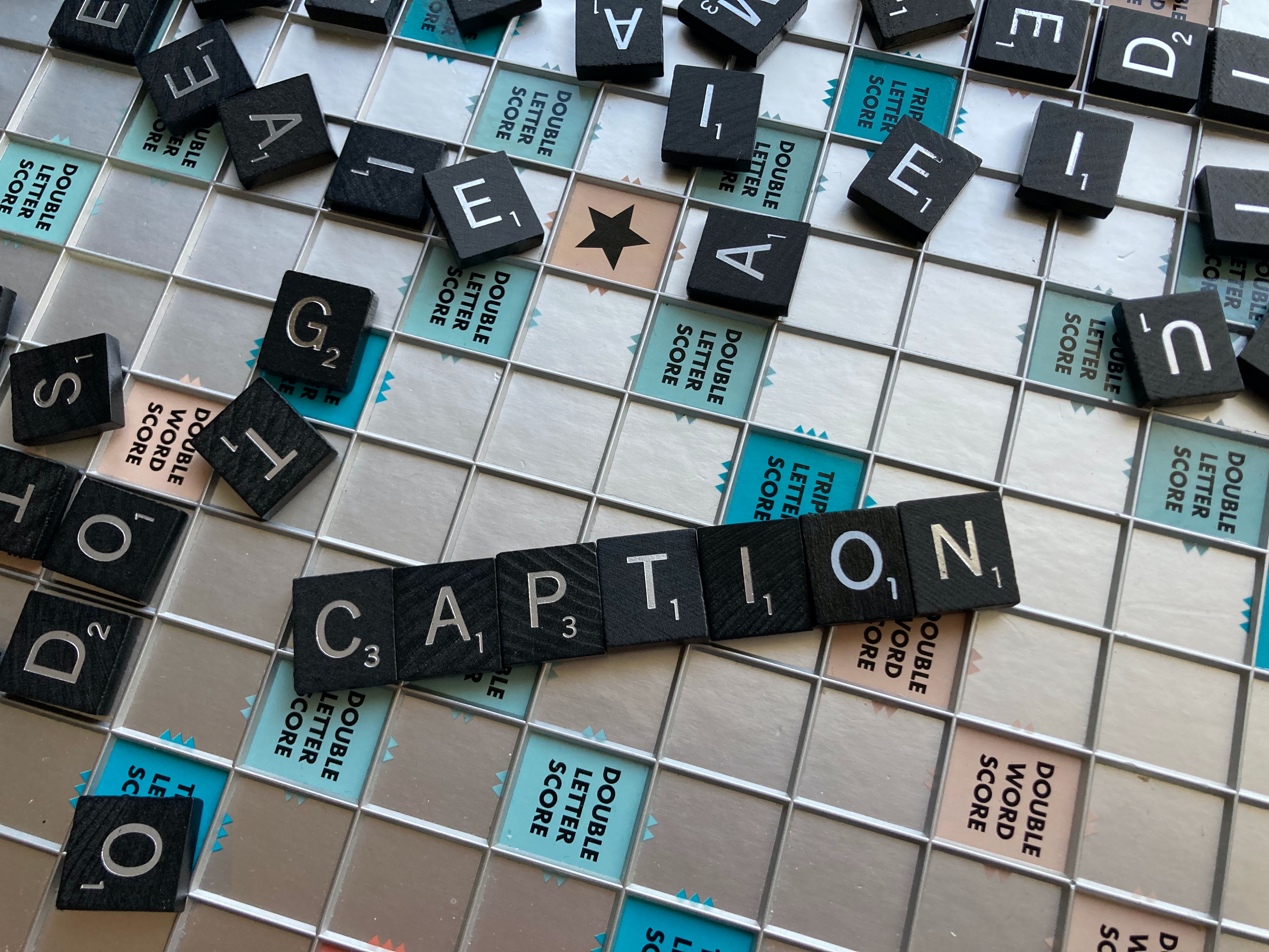 The word ‘caption’ spelled on a scrabble board surrounded by other letters.