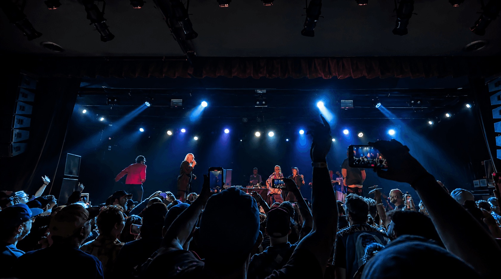 A crowd with phones raised at a concert, the stage lit in blue