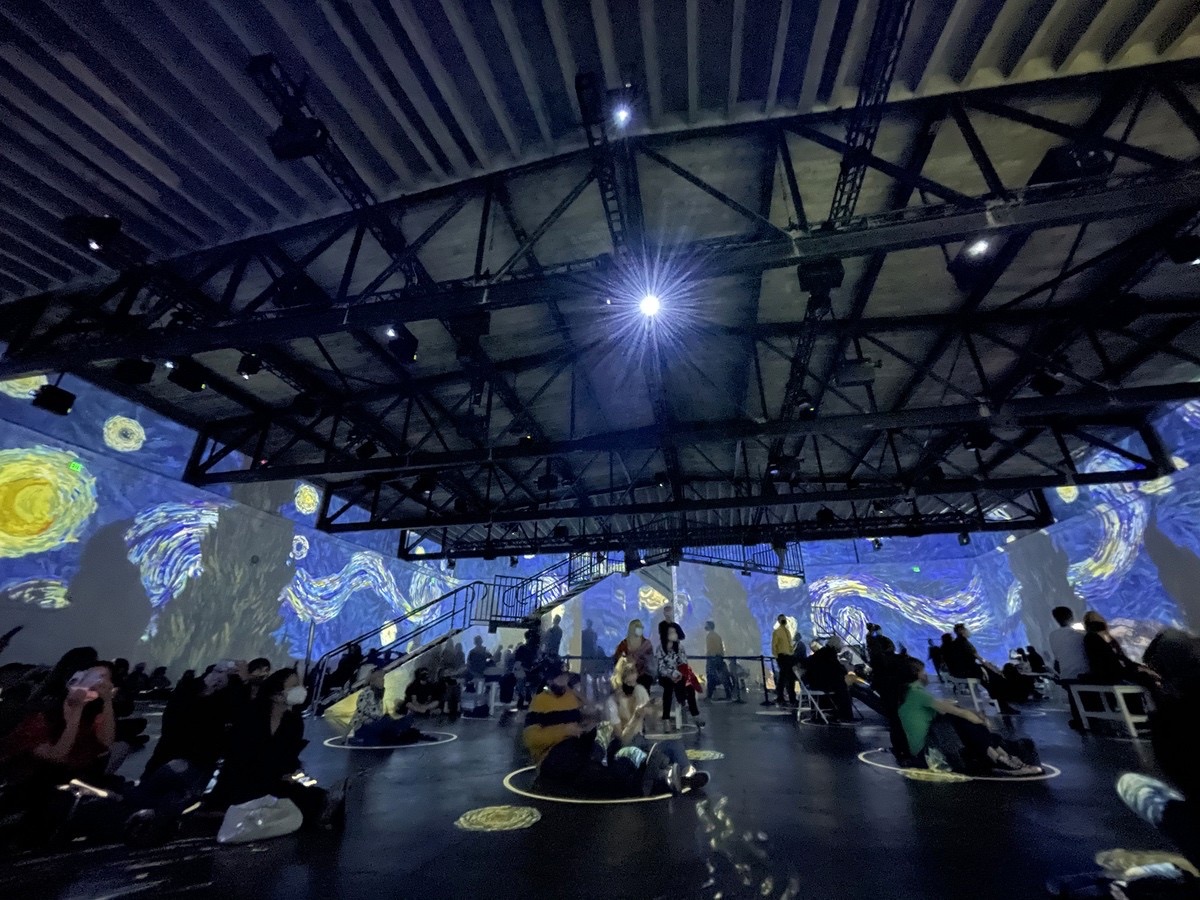 People sitting on the floor of an immersive Van Gogh exhibit, Starry Night projected around them