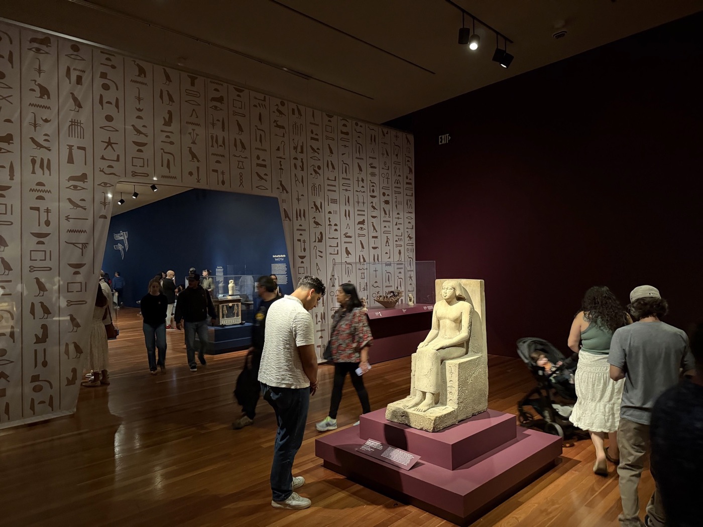 Visitors in a museum gallery of ancient Egyptian sculpture, hieroglyphs on the walls