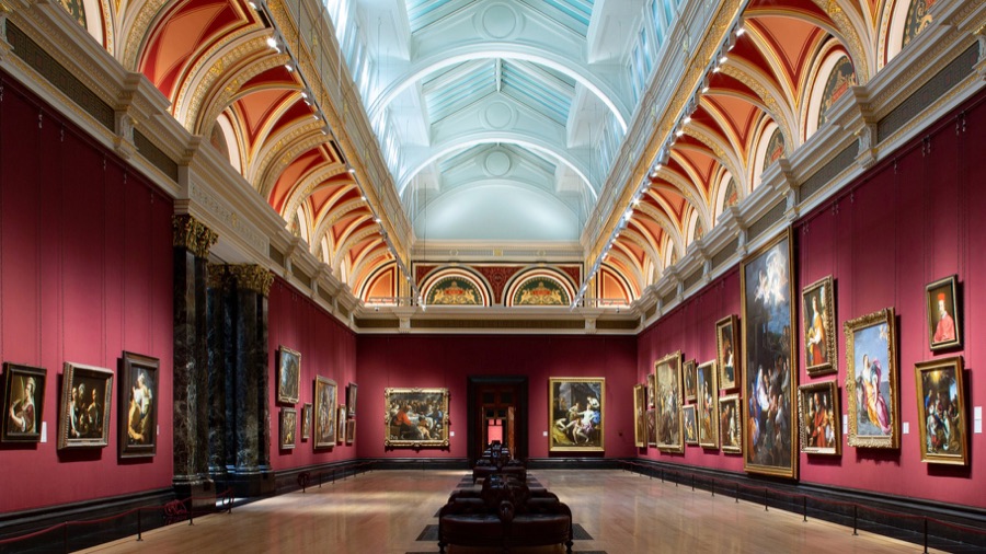 A long gallery of paintings under a skylit ceiling
