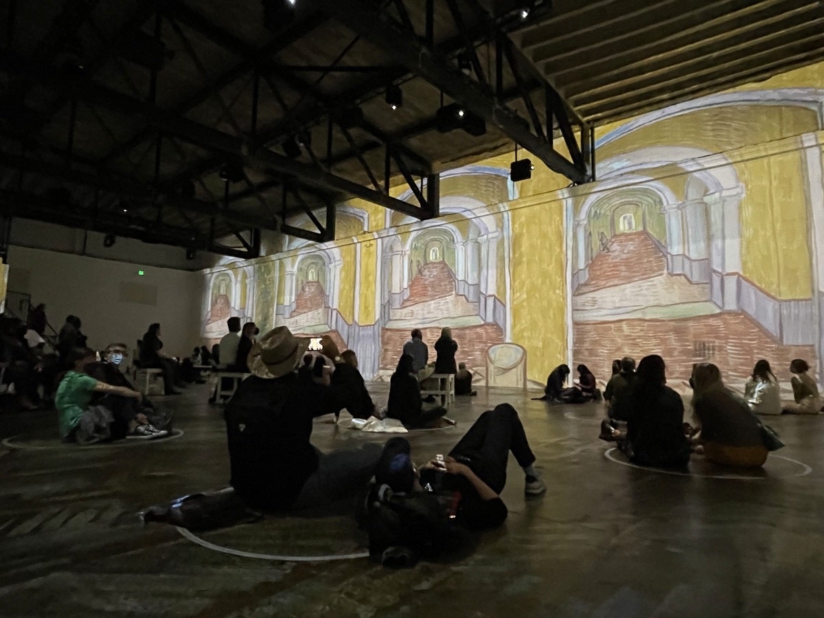 An audience watching a Van Gogh painting projected across a warehouse wall