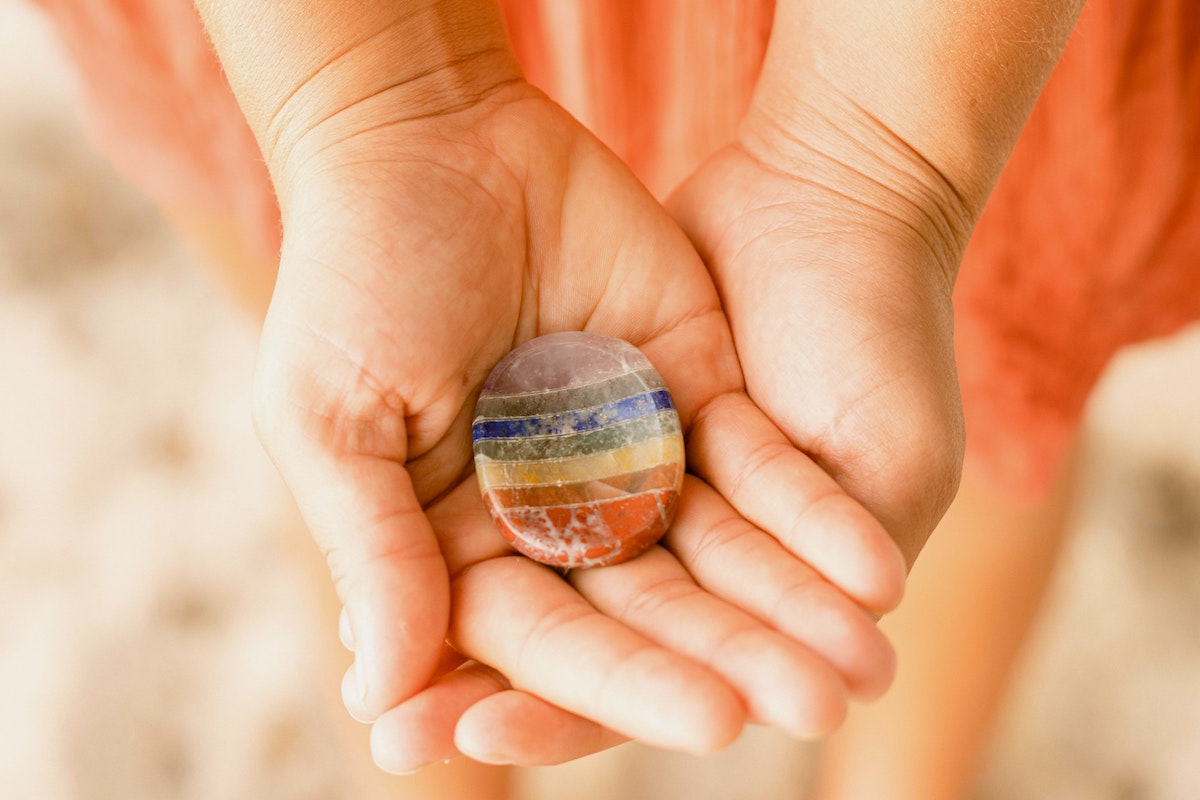 hands holding a plat rainbow stone