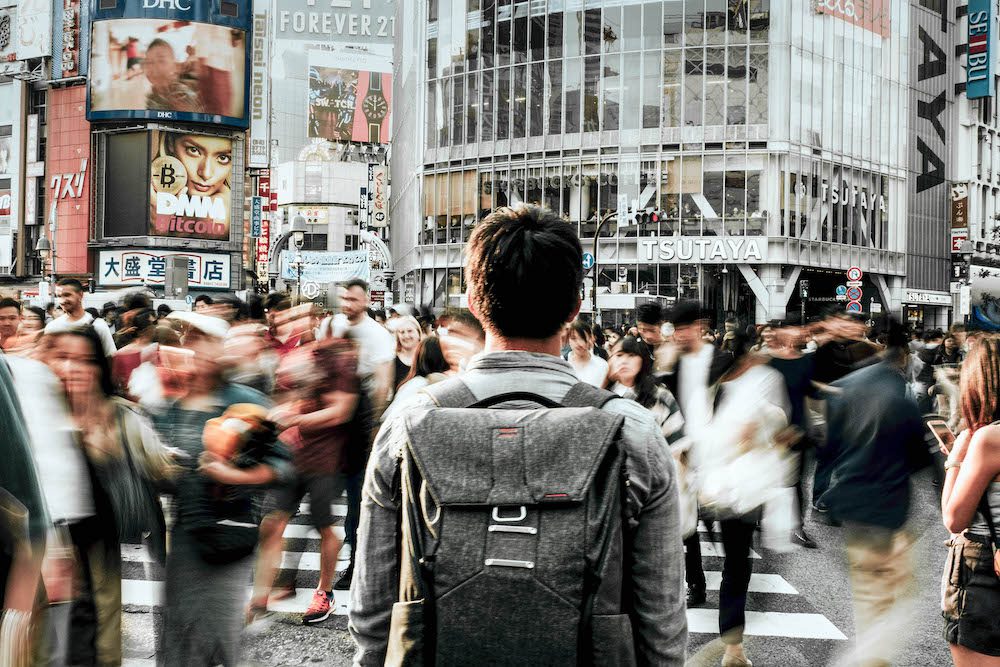 Backside of a man standing in a crowd and carrying a backpack trying to find out how to be yourself