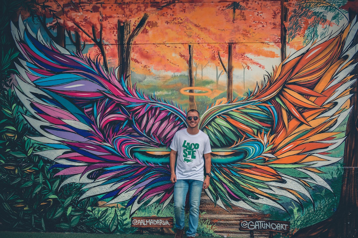 Man standing in front of a graffiti wall of wings
