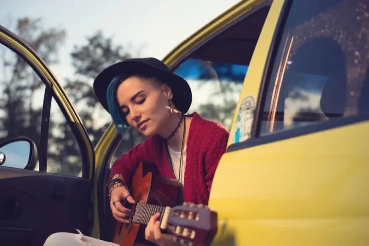 a girl sitting in the car and playing the guitar