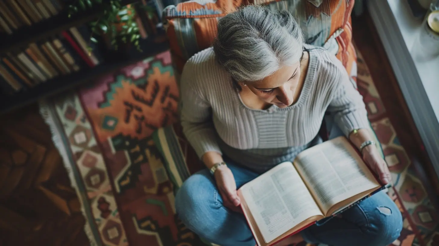 A silver-haired woman in a sweater and jeans reading a book while sitting on a colorful rug in a warm, book-filled room.