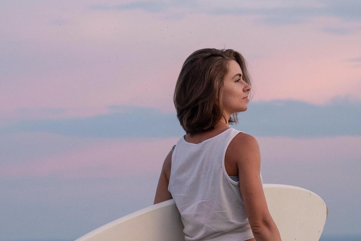 Woman holding a surfboard looking into the horizon and contemplating her life goals