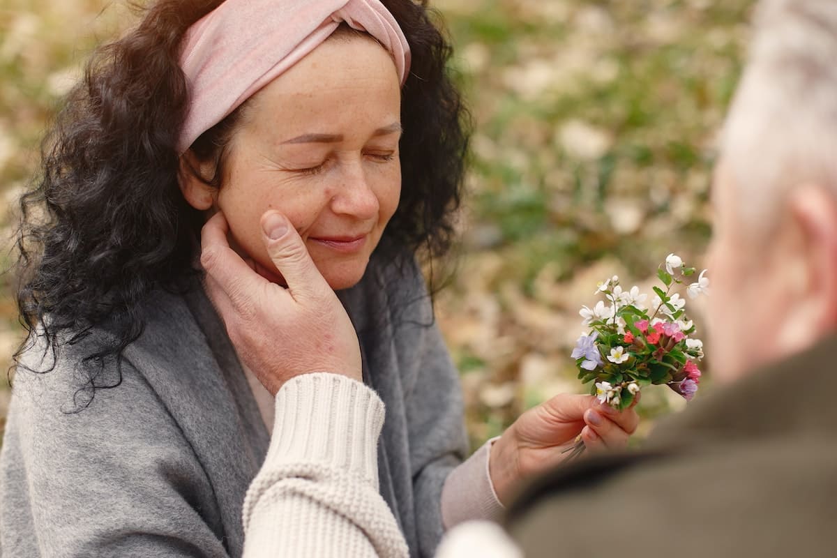 a woman holding flowers in her hand and a man stroking empathetically on her face