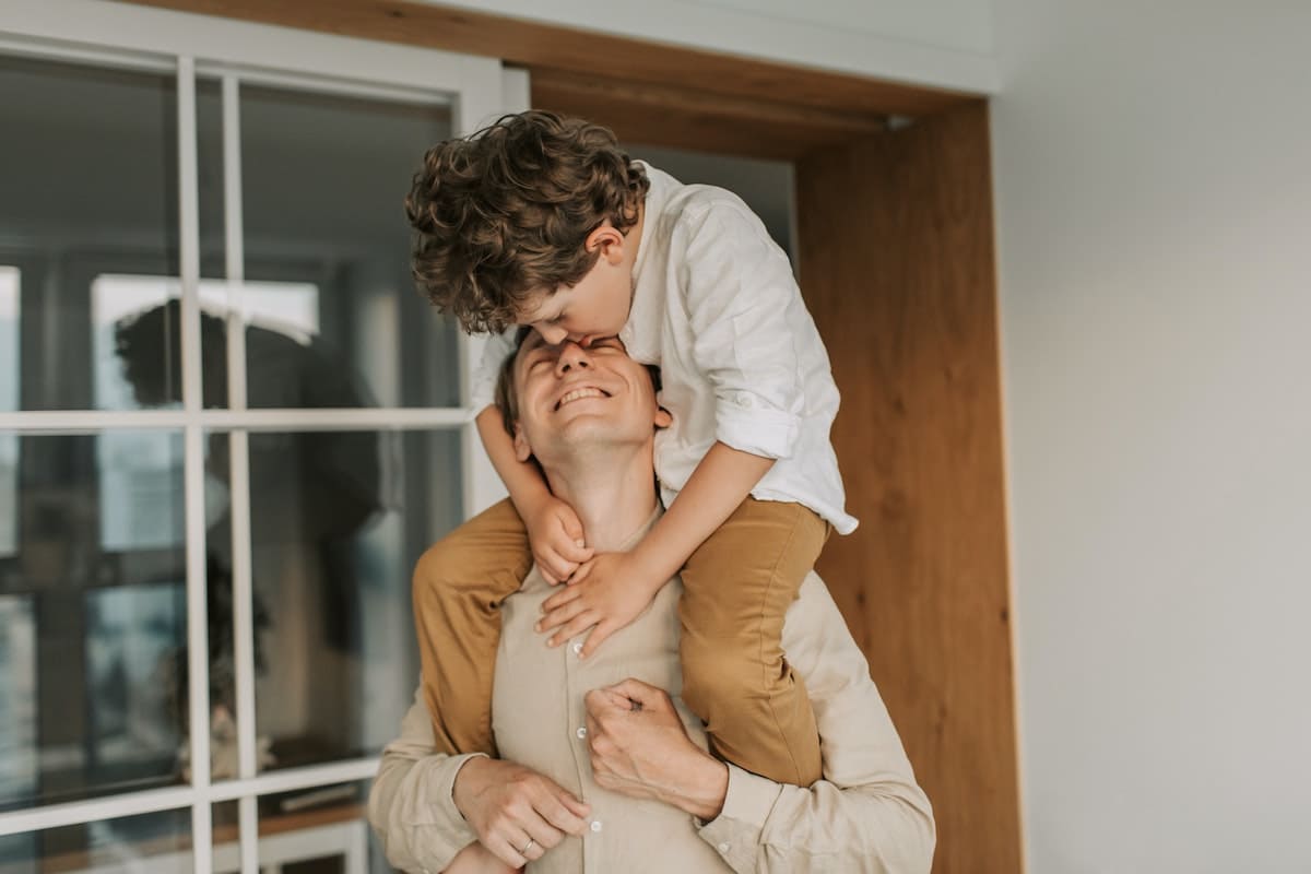 Son sitting on his father's shoulders and kissing his face