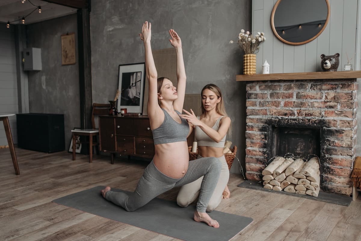 a female yoga instructor assisting a pregnant woman in yoga posture