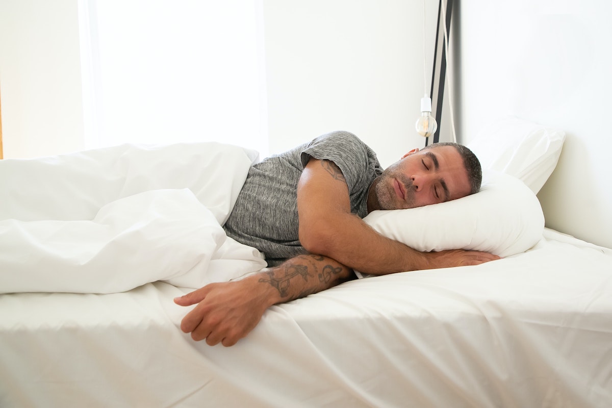 Man sleep on his side in bed as a way to learn how to fix sleep schedule.