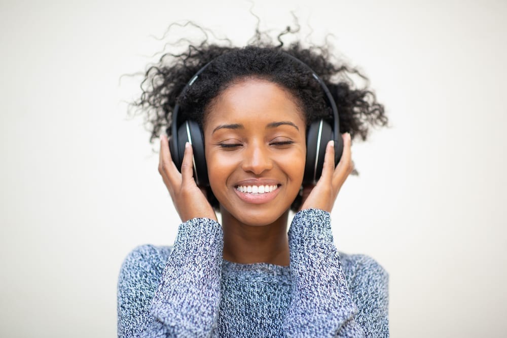 Close up front portrait young african american woman listening to music with headphones and eyes closed