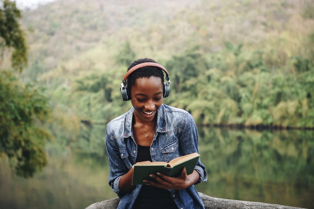 Woman reading a book in nature while listening to podcast