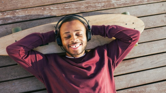 Young man listening podcasts with headphone outside.