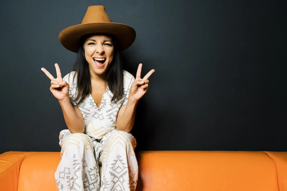 Miki Agrawal sitting on an orange couch and giving the peace sign