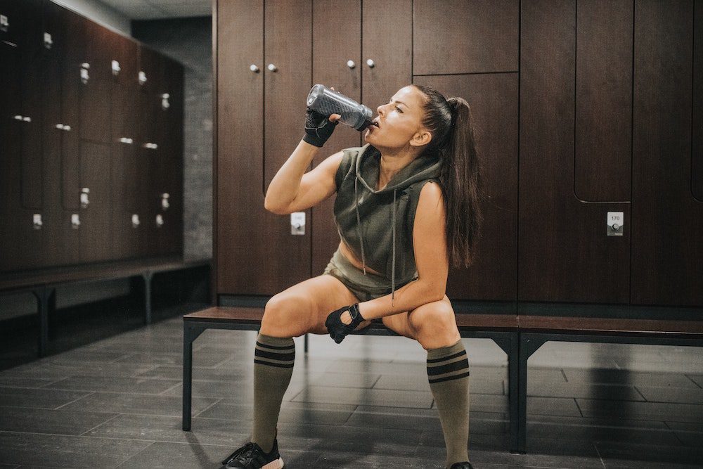 Athletic woman drinking water in locker room for a healthy vaginal microbiome
