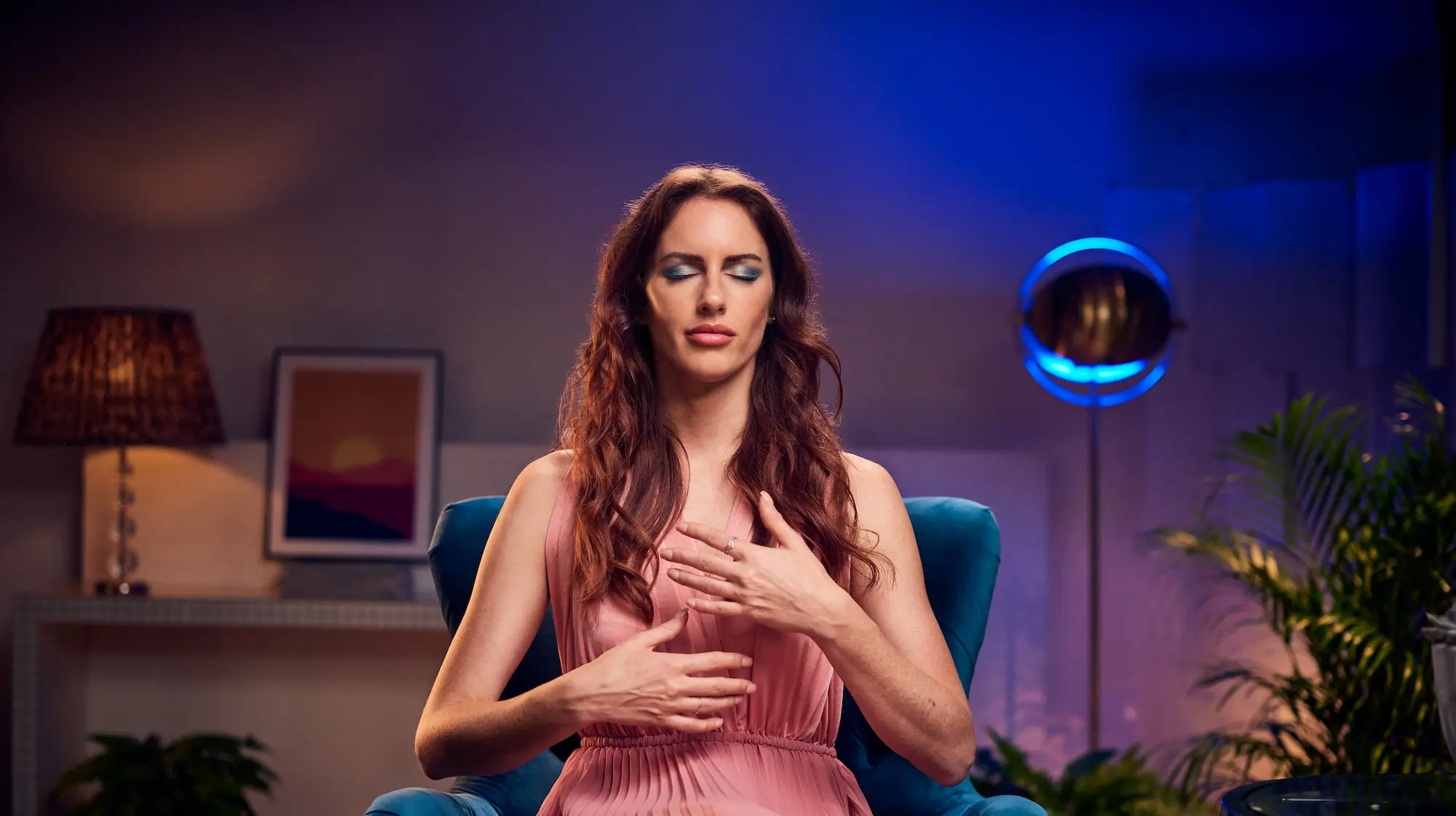 Jade Shaw, trainer of Mindvalley’s The Art of Astral Projection program, sits with eyes closed and hands on chest, practicing a meditative breathing technique in a softly lit room.