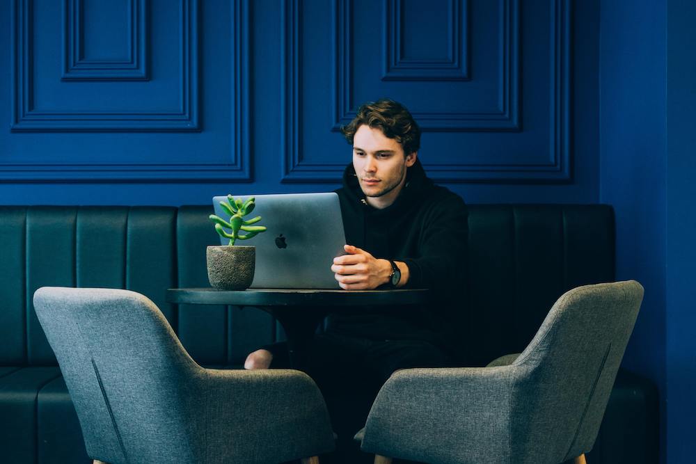 Man working on laptop in front of a blue wall