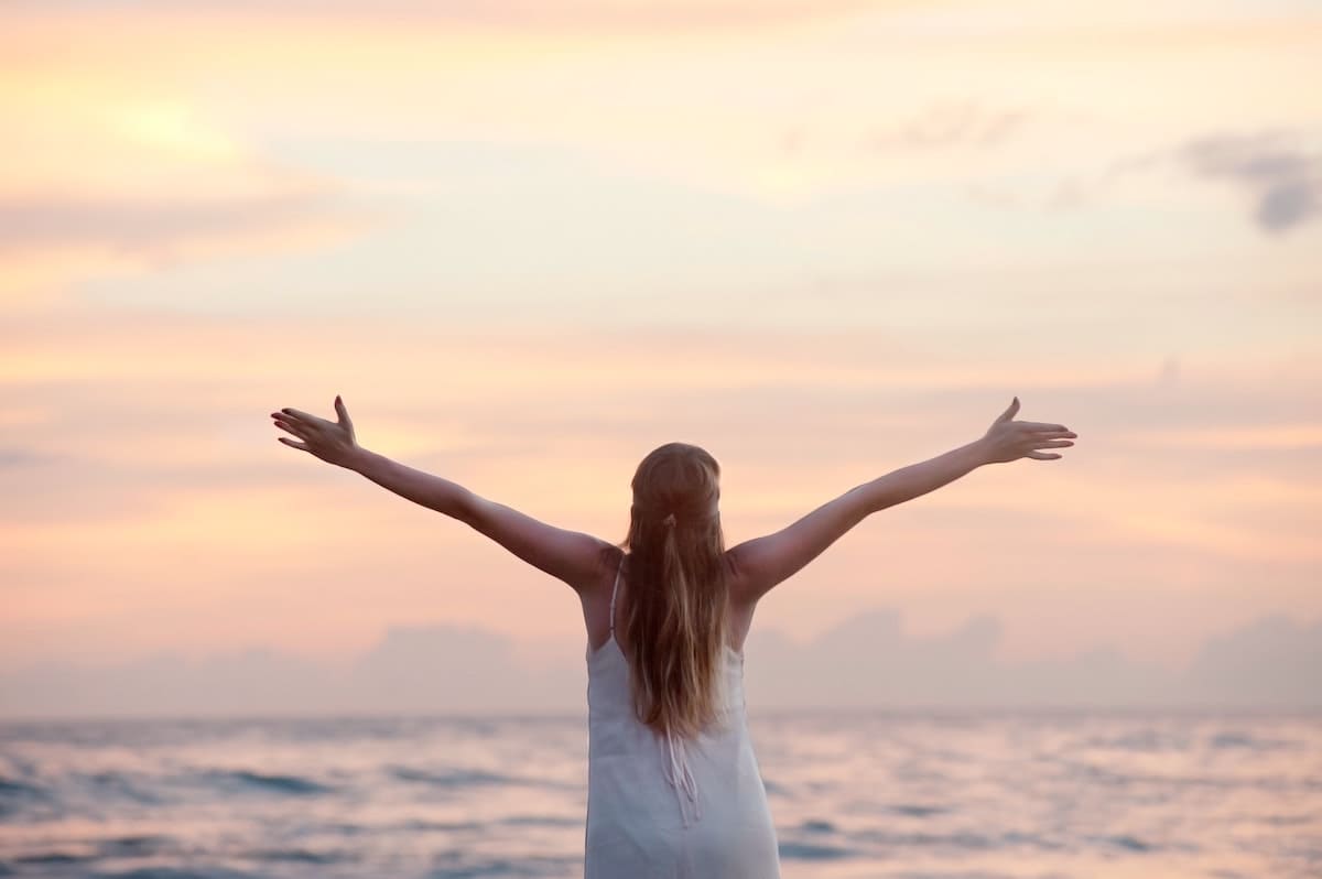 woman standing in front of the ocean with her arms wide open