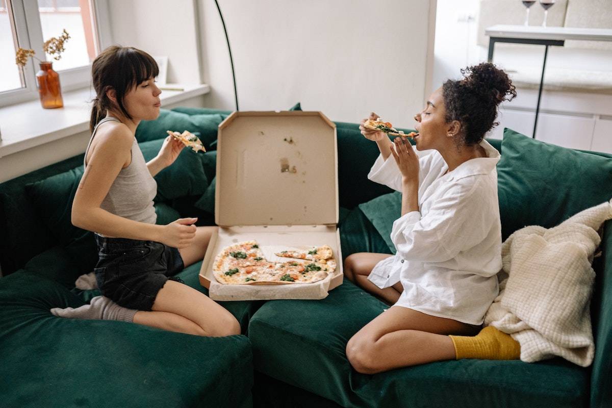 Women eating a pizza on the couch to show how the food industry is failing us