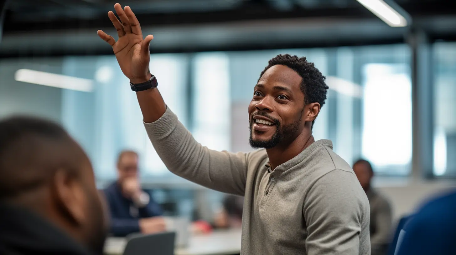 A man in a grey shirt smiles as he raises his hand in an office setting