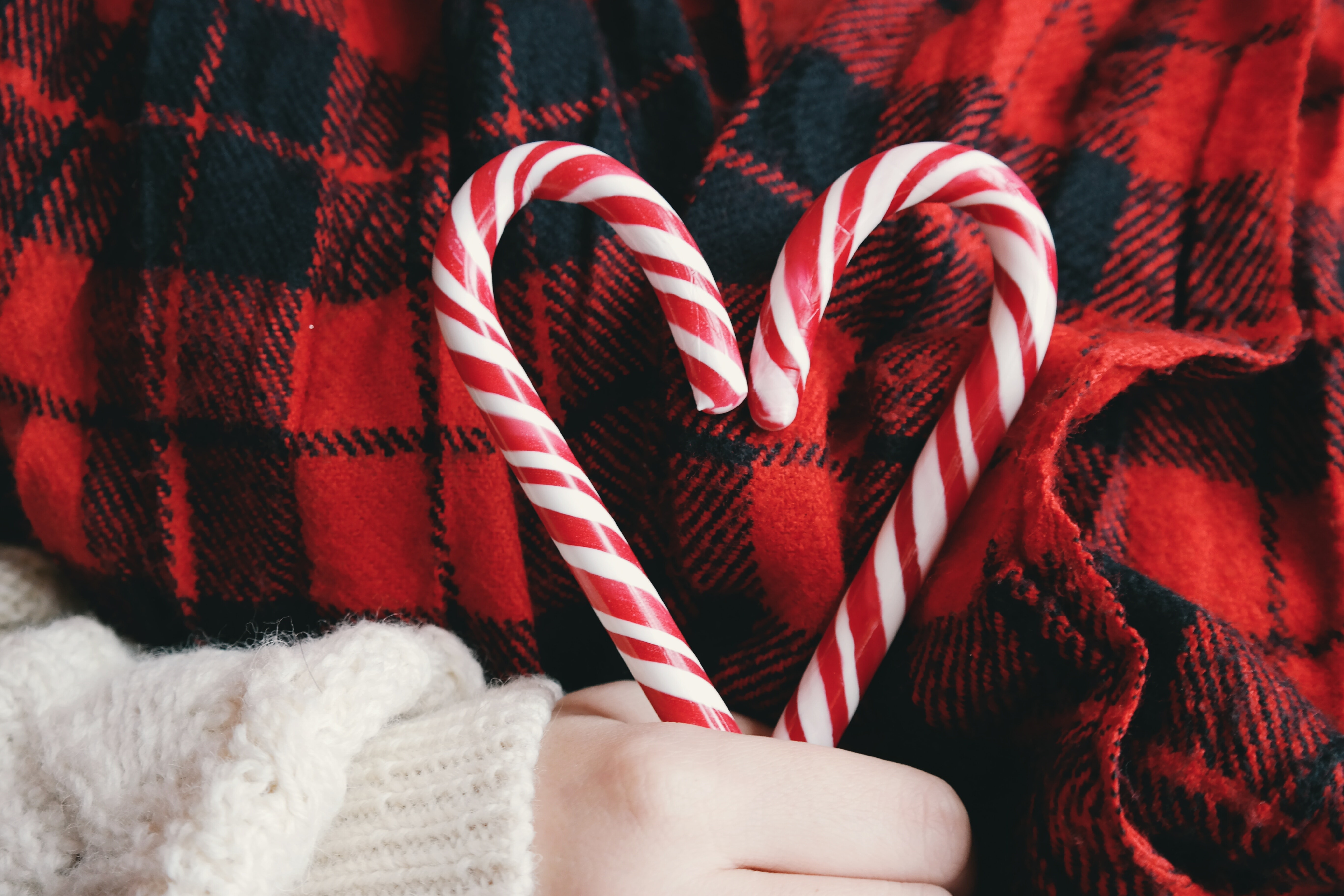 Child wearing red/black flannel holding two candy canes making heart 