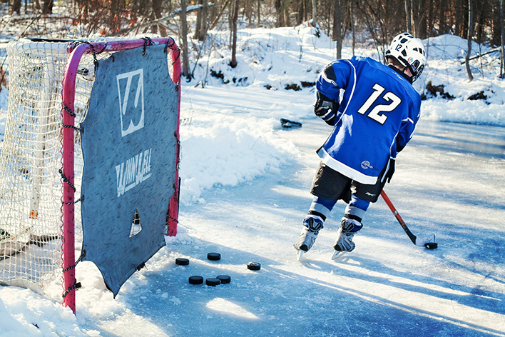 Kid playing hockey outdoors in the snow with red goal