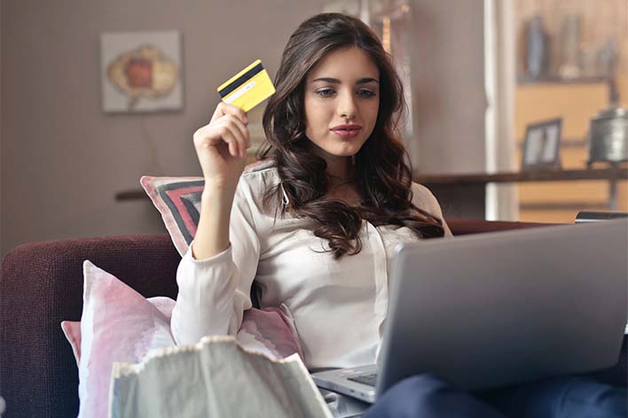 Woman holding credit card sitting on couch with laptop in lap