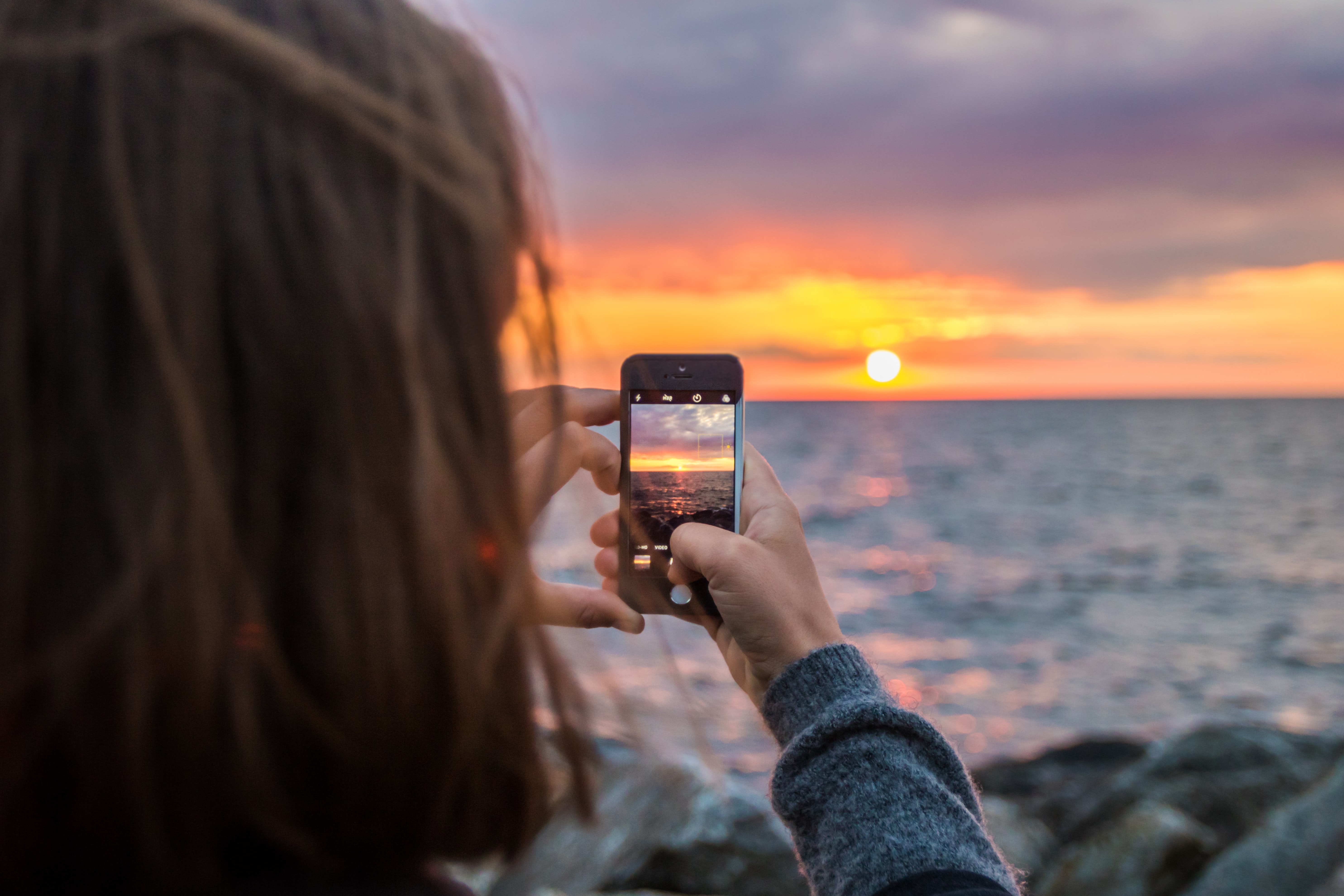 Woman using camera phone to take picture of sunset