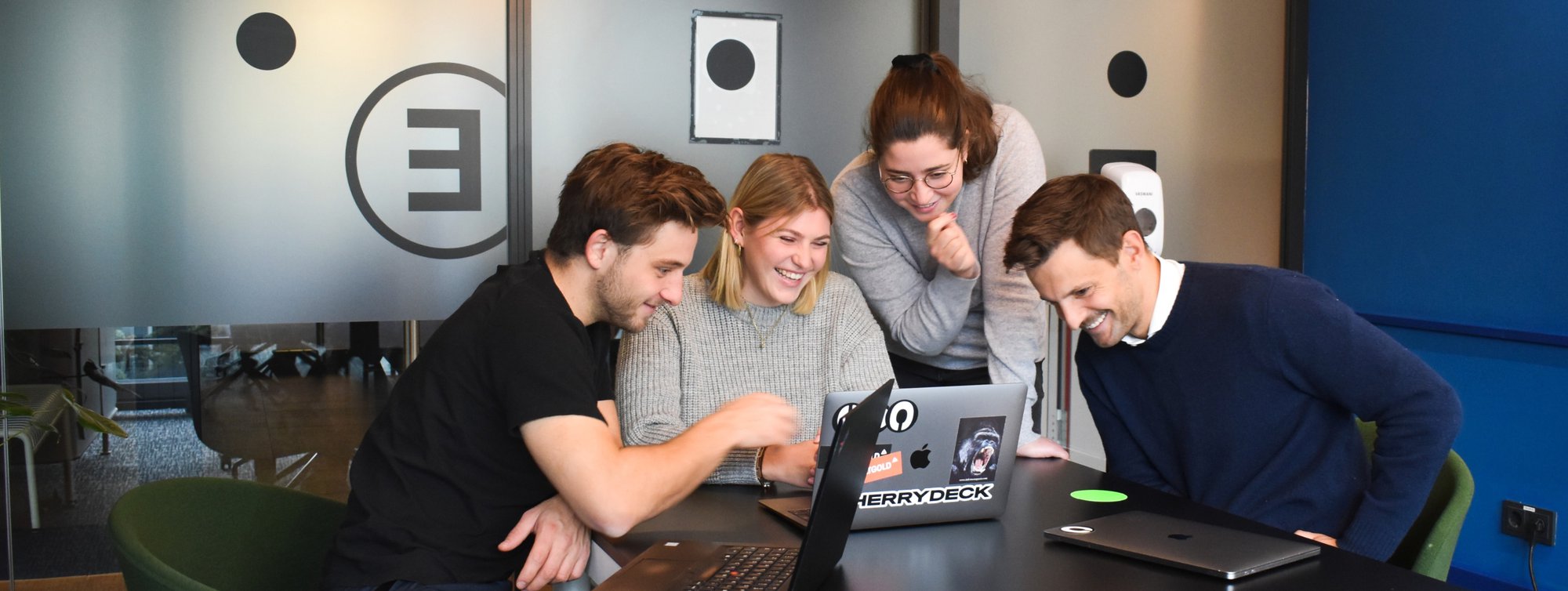 4 people looking at a laptop and laughing