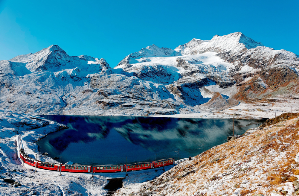 Un treno Bernina Express viaggia lungo la riva del lago Bianco