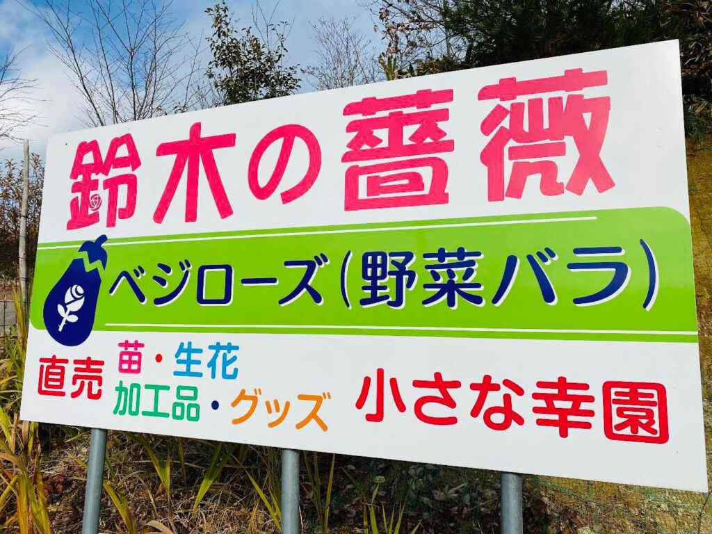 鈴木の薔薇の看板「鈴木の薔薇 べジローズ（野菜バラ）直売 苗・生花・加工品・グッズ　小さな幸園」と書いてある