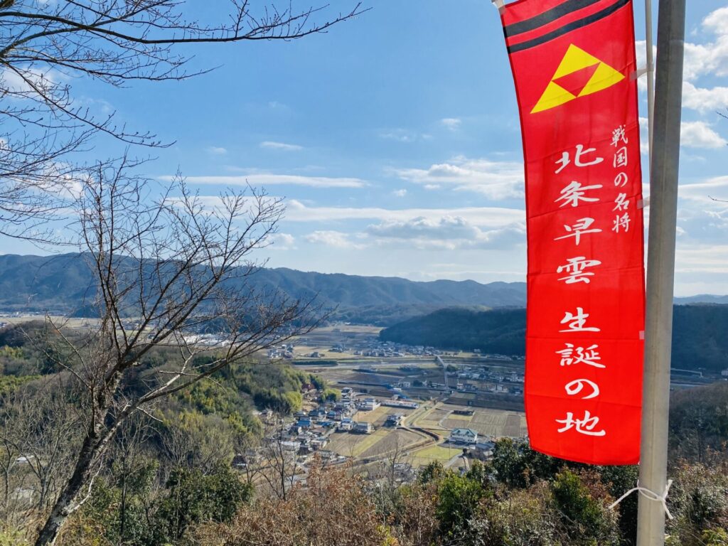 山の上から見た街並み、右側に旗が立っている、戦国の名将 北条早雲 生誕の地と書いてある