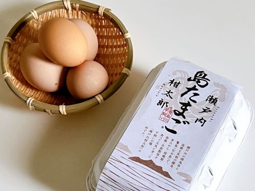 木目調の網籠の中に島たまごが4つ入っている。隣には島たまごが入っていたパッケージが置かれている。パッケージには、瀬戸内の離島、佐木島のイラストが上品にデザインされている。