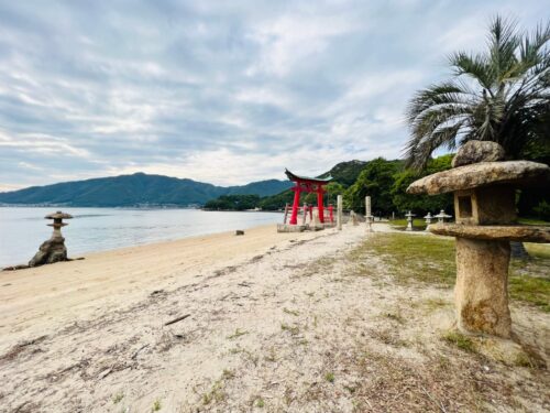 手前に石灯篭、奥に鳥居が見える海岸線から撮影した写真