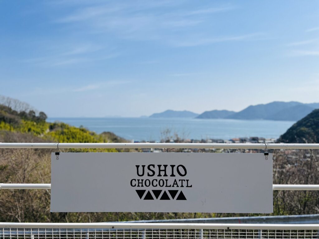 瀬戸内海をバックに看板を撮影、「USHIO CHOCOLATL」と書いてある