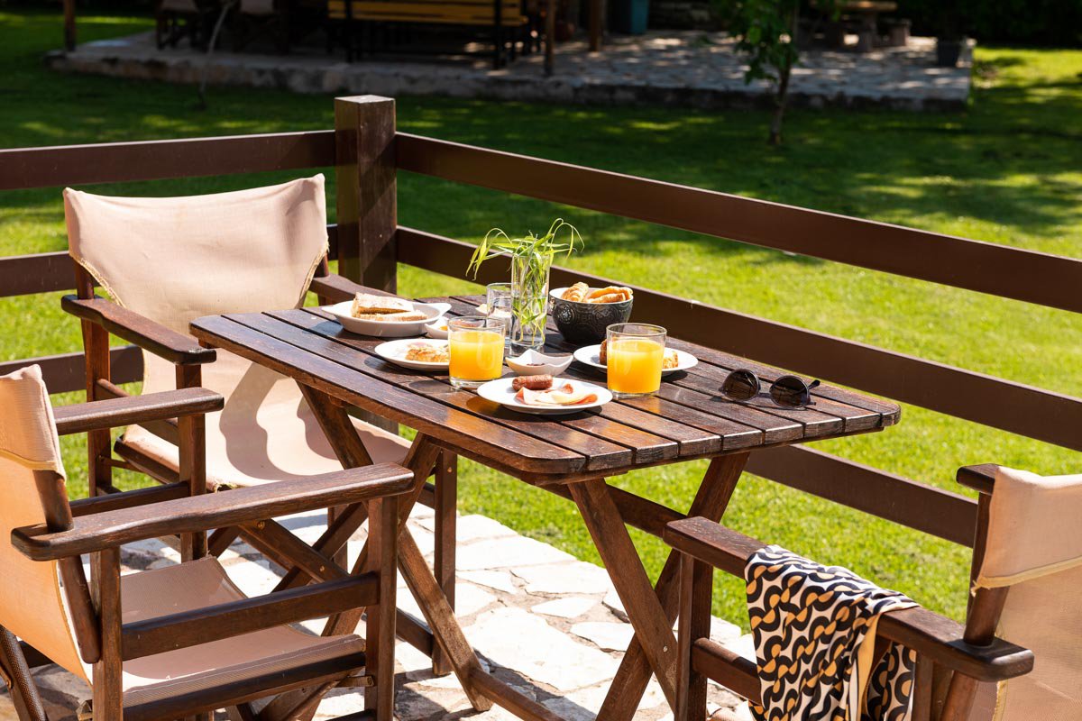 Ένα ξύλινο τραπέζι και καρέκλες σε μια βεράντα με φαγητό και ποτά.