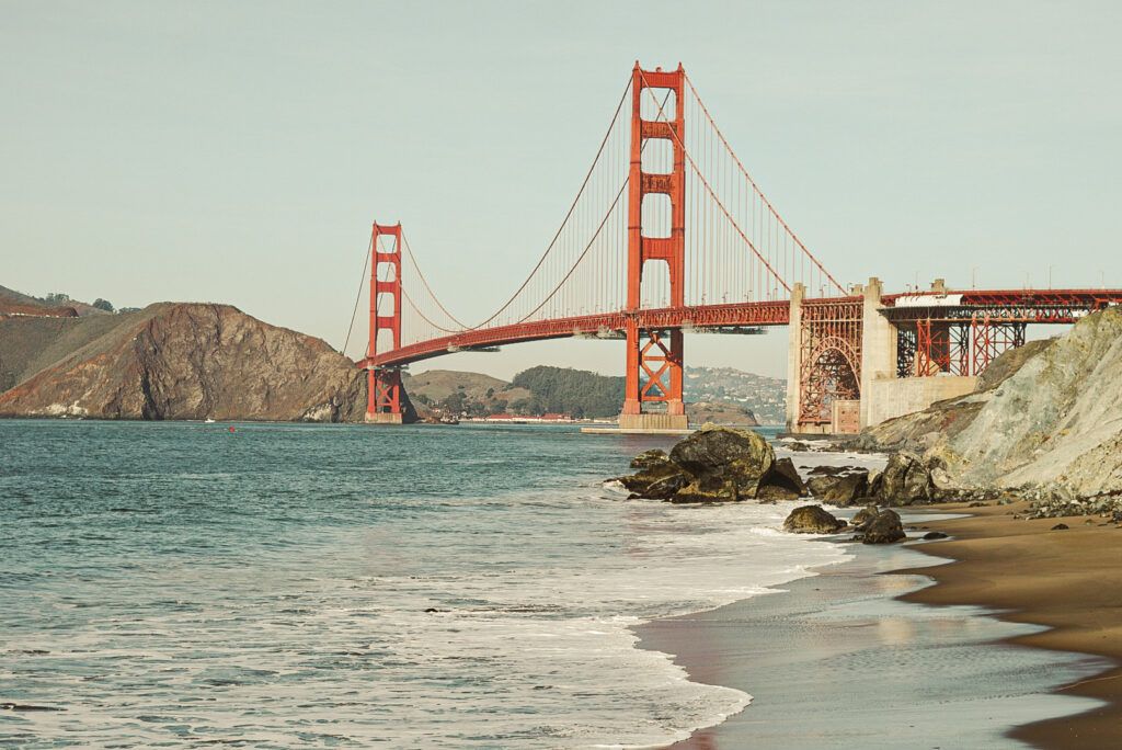 Picture of the Golden Gate Bridge in San Francisco in the background, water on the shore in foreground