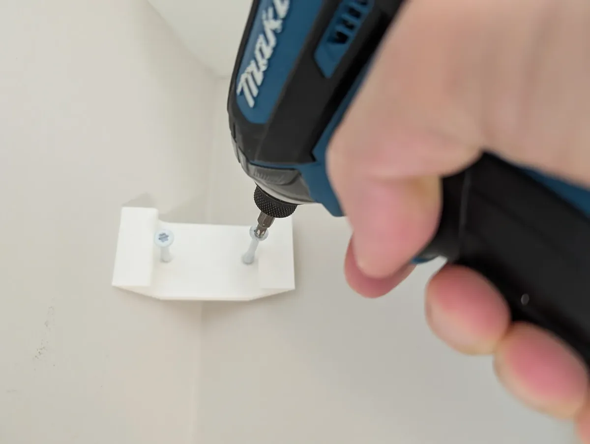 Driving a wood screw through a cleat into a wall stud near the ceiling