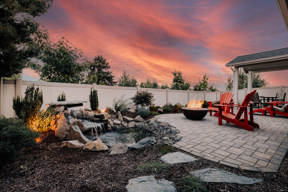 Waterfall feeding into a pond next to a fire put under a pink and blue sunset