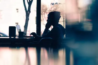 Silhouette of a person sitting in a coffee shop with a laptop