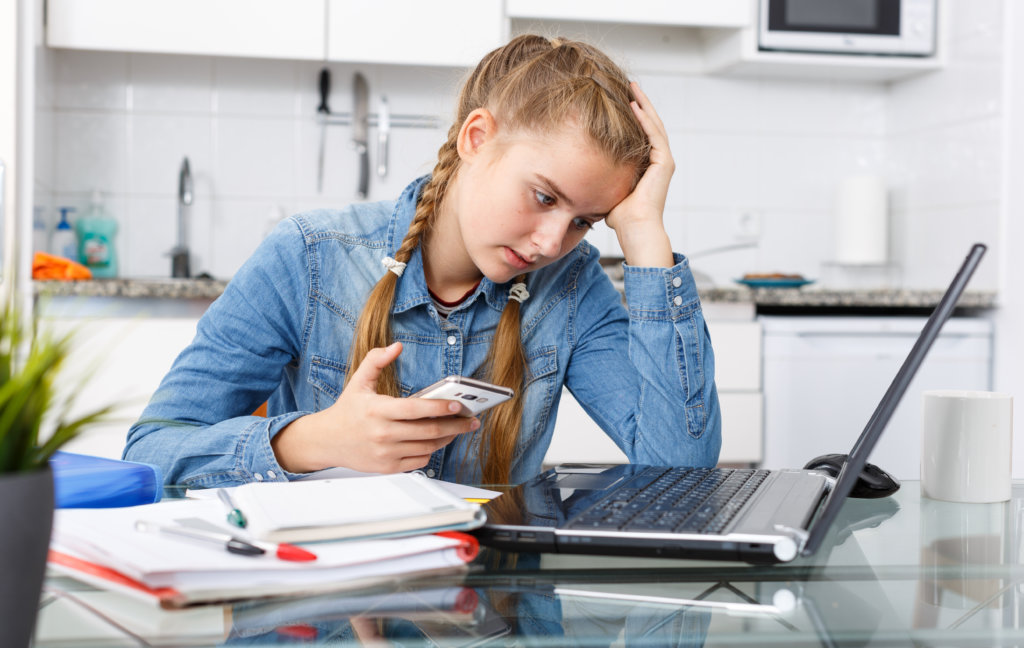 Imagem mostra menina em uma mesa com notebook e livros estudando através do Ensino Online.
