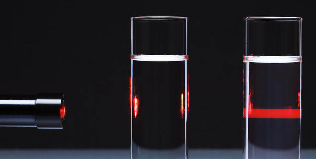 Um laser vermelho passa por duas soluções de composições diferentes. A primeira não espalha a luz, pois de uma solução verdadeiramente homogênea. A segunda solução é um coloide, espalhando em seu meio a luz incidida.