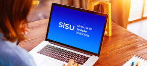 Uma pessoa está usando um laptop que exibe na tela a página inicial das notas de corte do SiSU, Sistema de Seleção Unificada, em um ambiente interno bem iluminado.