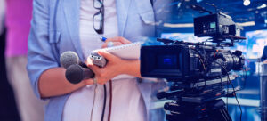 Imagem mostra uma câmera de televisão e parte do corpo de uma repórter segurando um caderno de anotações, celular e microfones