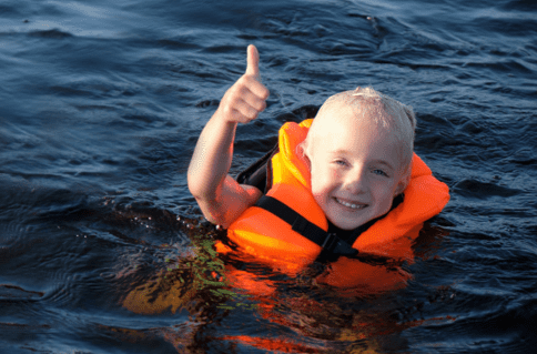 Menino loiro com colete salva-vidas laranja boiando na água