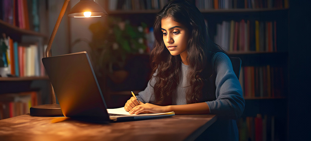 Uma jovem estudante desenvolvendo sua autodisciplina escrevendo em um caderno à mesa sob a luz de uma lâmpada, com um laptop aberto à sua frente