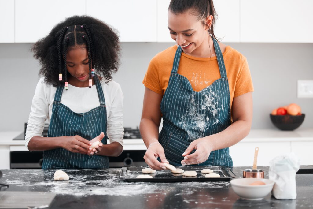 Duas jovens, ambas usando aventais, estão preparando cookies em uma cozinha