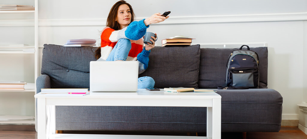 Adolescente sentada no sofá assistindo televisão e praticando a autossabotagem